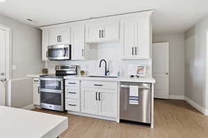 Contemporary kitchen featuring white cabinetry, stainless steel appliances, a subway tile backsplash, solid surface countertops, and wood-finish flooring