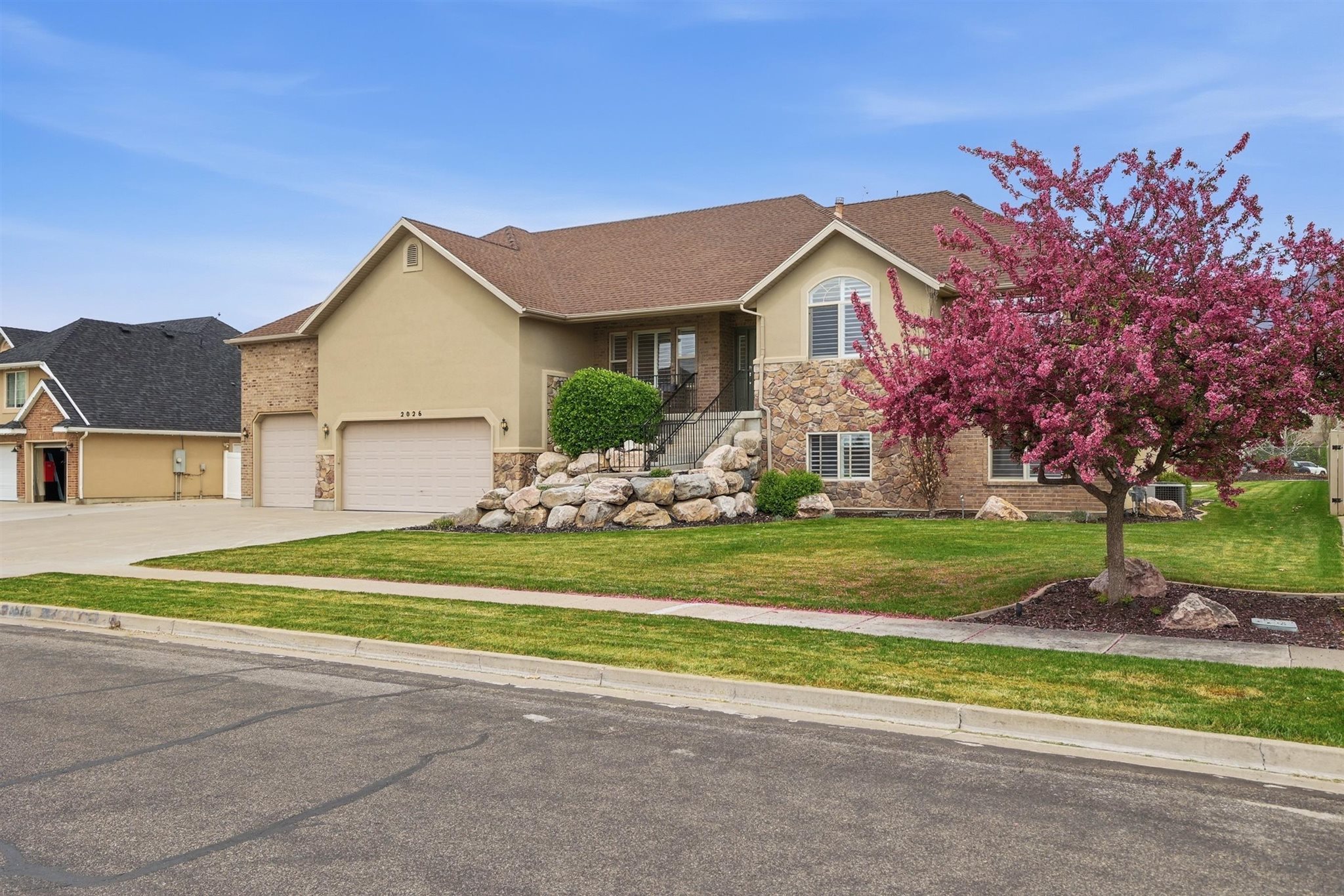 Stucco and stone facade home featuring a two-car garage, established front yard landscaping, and a vibrant blossoming tree