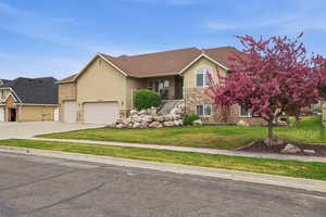 Stucco and stone facade home featuring a two-car garage, established front yard landscaping, and a vibrant blossoming tree