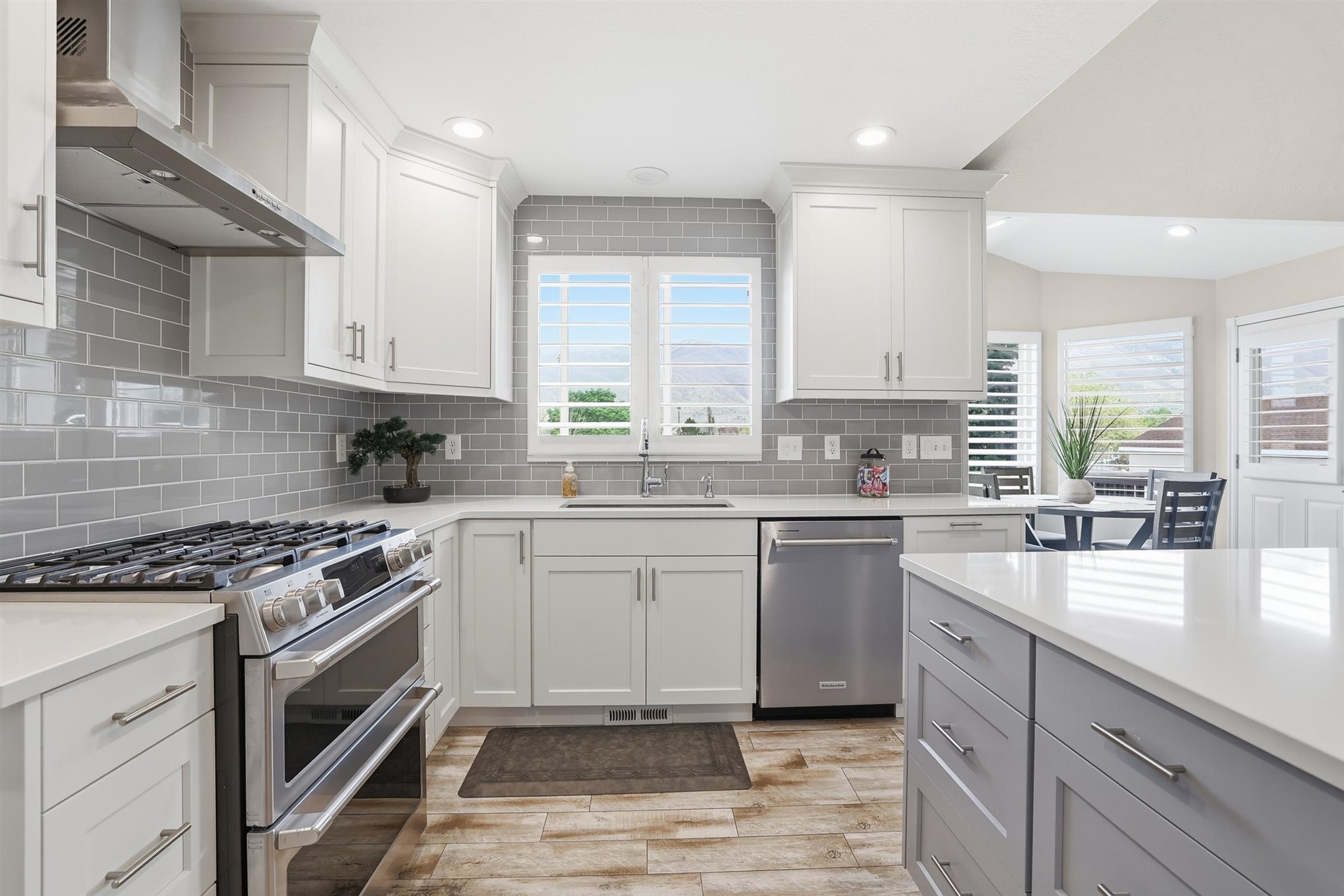 Modern kitchen featuring white upper cabinetry, a grey subway tile backsplash, and a large stainless steel range with a coordinating vent hood