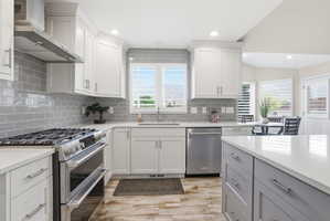 Modern kitchen featuring white upper cabinetry, a grey subway tile backsplash, and a large stainless steel range with a coordinating vent hood
