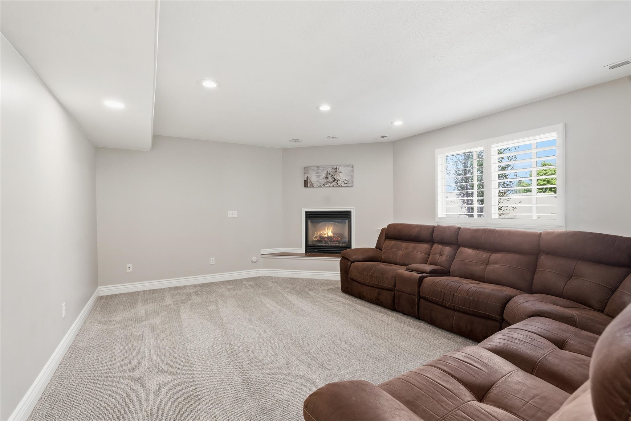 Recessed lighting illuminates a carpeted living space featuring a corner fireplace with a raised hearth