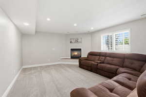 Recessed lighting illuminates a carpeted living space featuring a corner fireplace with a raised hearth