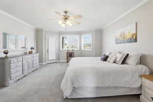 Carpeted bedroom featuring a ceiling fan with integrated lighting, crown molding, bay windows with plantation shutters, and a glass-paneled door