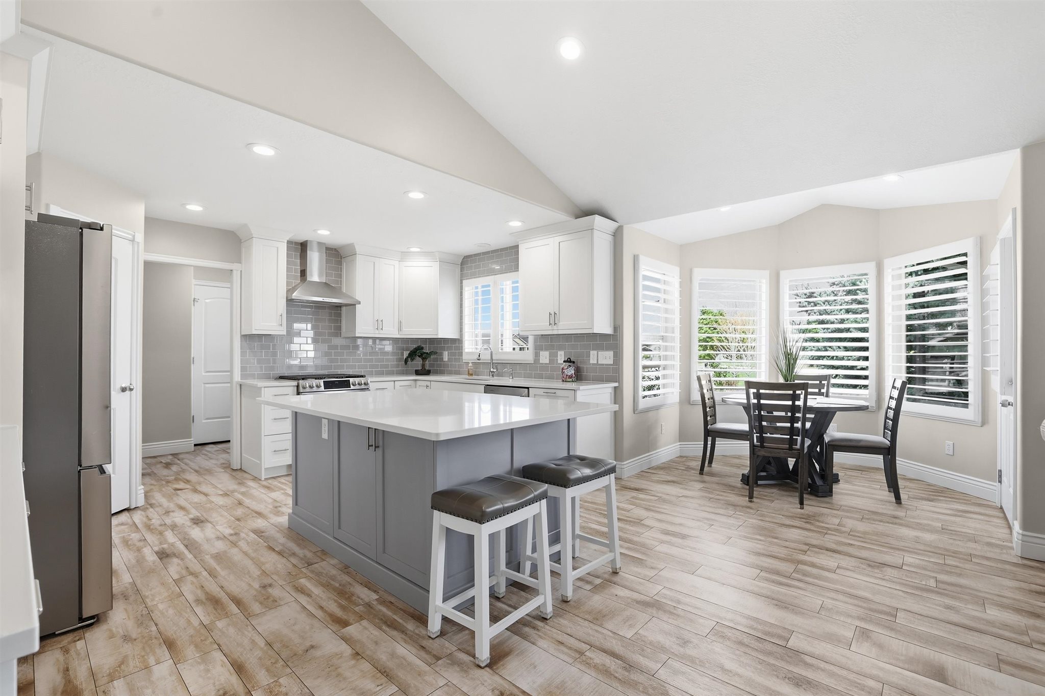 Contemporary kitchen featuring an expansive center island with seating, white shaker cabinetry, stainless steel appliances, and a subway tile backsplash