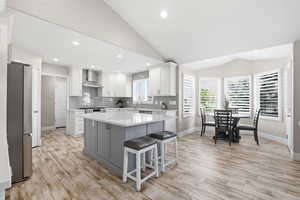 Contemporary kitchen featuring an expansive center island with seating, white shaker cabinetry, stainless steel appliances, and a subway tile backsplash