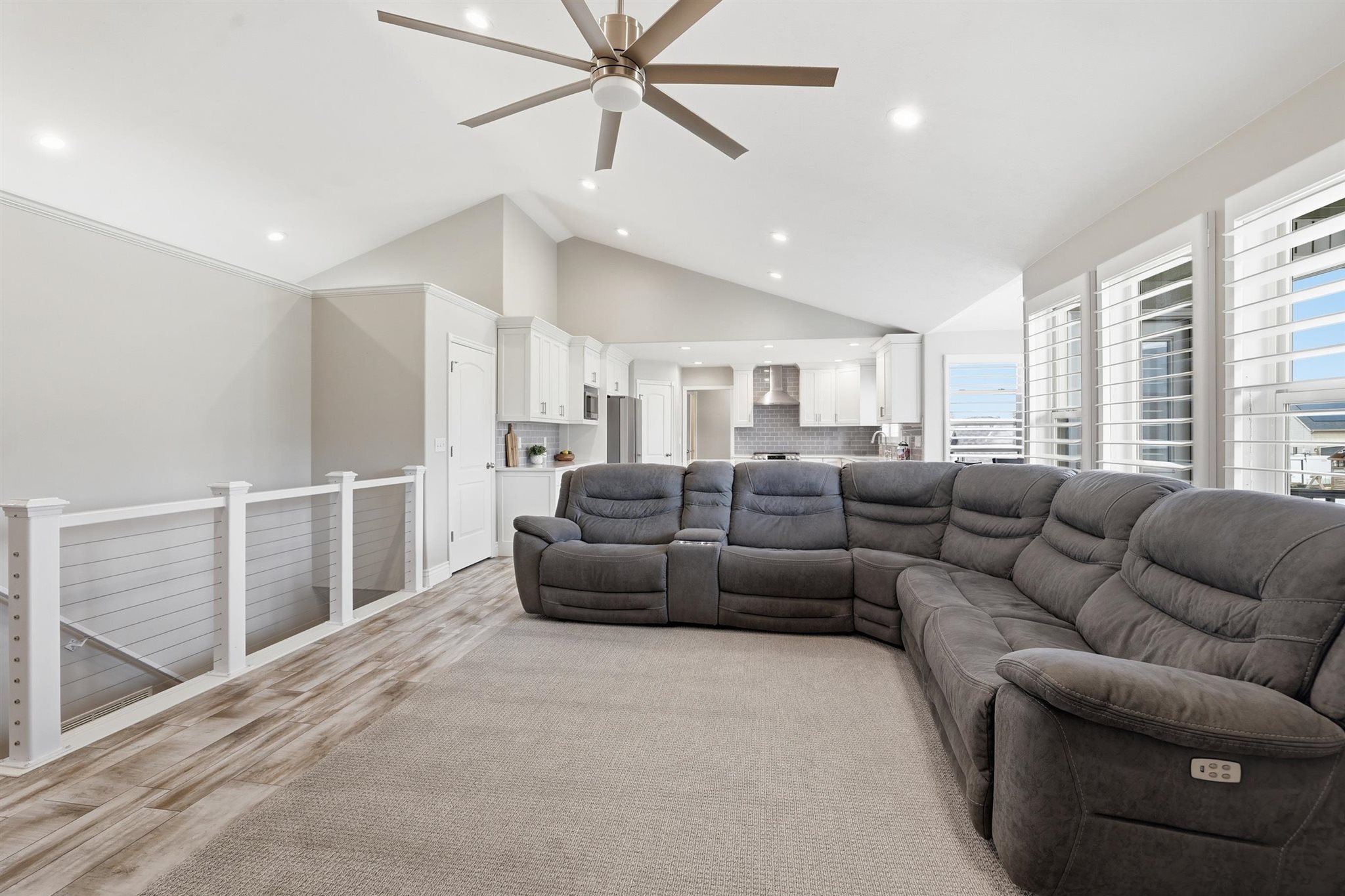 Open-concept living area featuring vaulted ceilings with a ceiling fan, recessed lighting, and wood-finish flooring extending into the kitchen