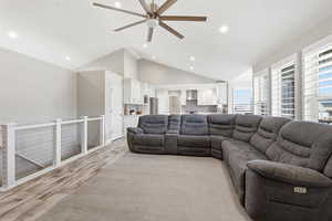 Open-concept living area featuring vaulted ceilings with a ceiling fan, recessed lighting, and wood-finish flooring extending into the kitchen