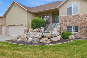 Stucco and stone exterior featuring a two-car garage, arched window, and rock retaining wall with mature landscaping