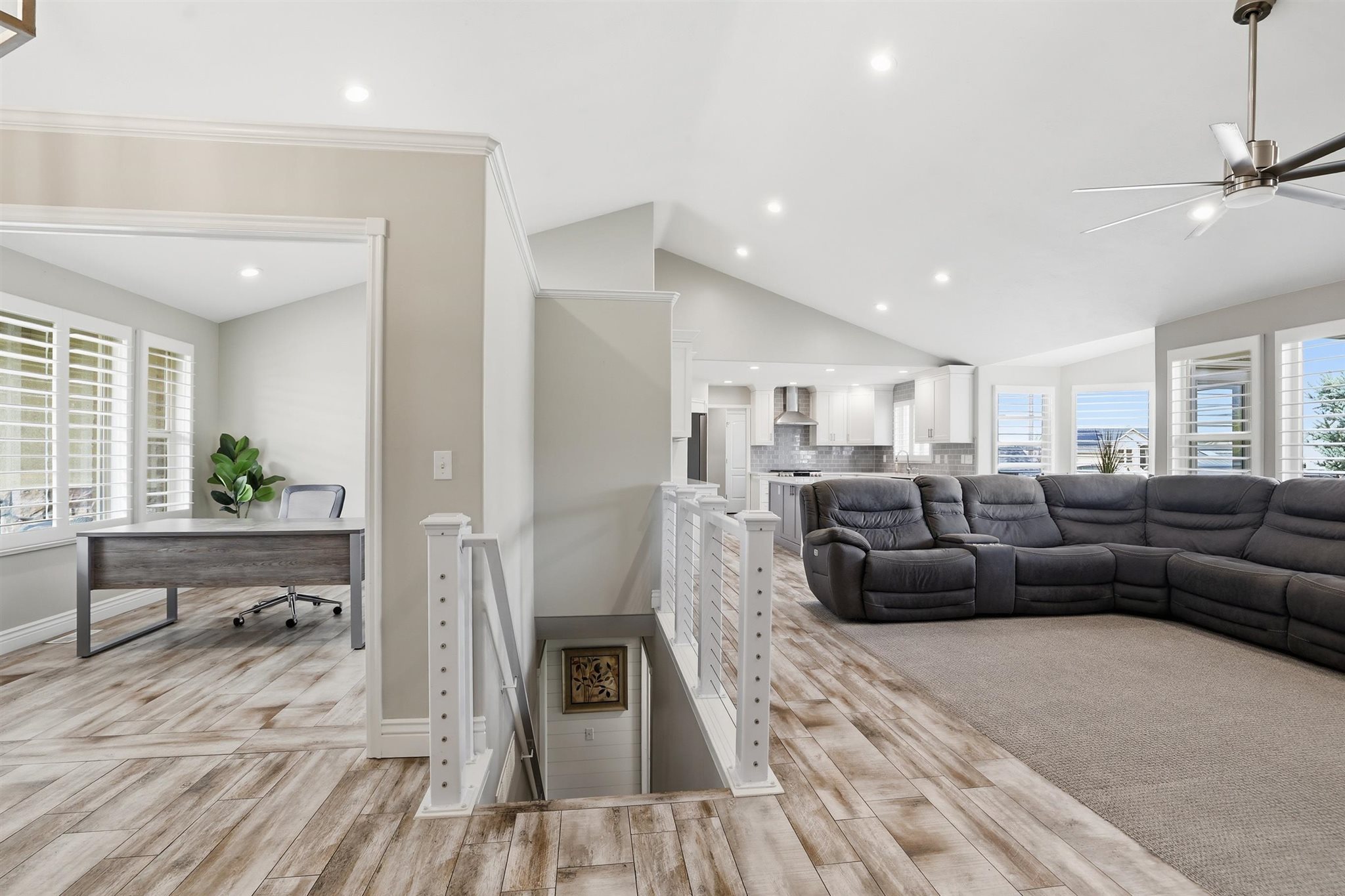 Open-concept living area featuring wood-finish flooring, vaulted ceilings, recessed lighting, and a modern ceiling fan