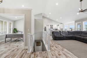 Open-concept living area featuring wood-finish flooring, vaulted ceilings, recessed lighting, and a modern ceiling fan