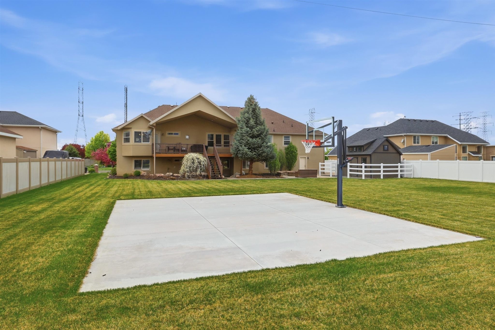 Expansive backyard featuring a concrete sports court with a basketball hoop, established lawn, and multi-level deck with stairs