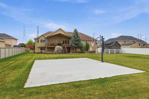 Expansive backyard featuring a concrete sports court with a basketball hoop, established lawn, and multi-level deck with stairs