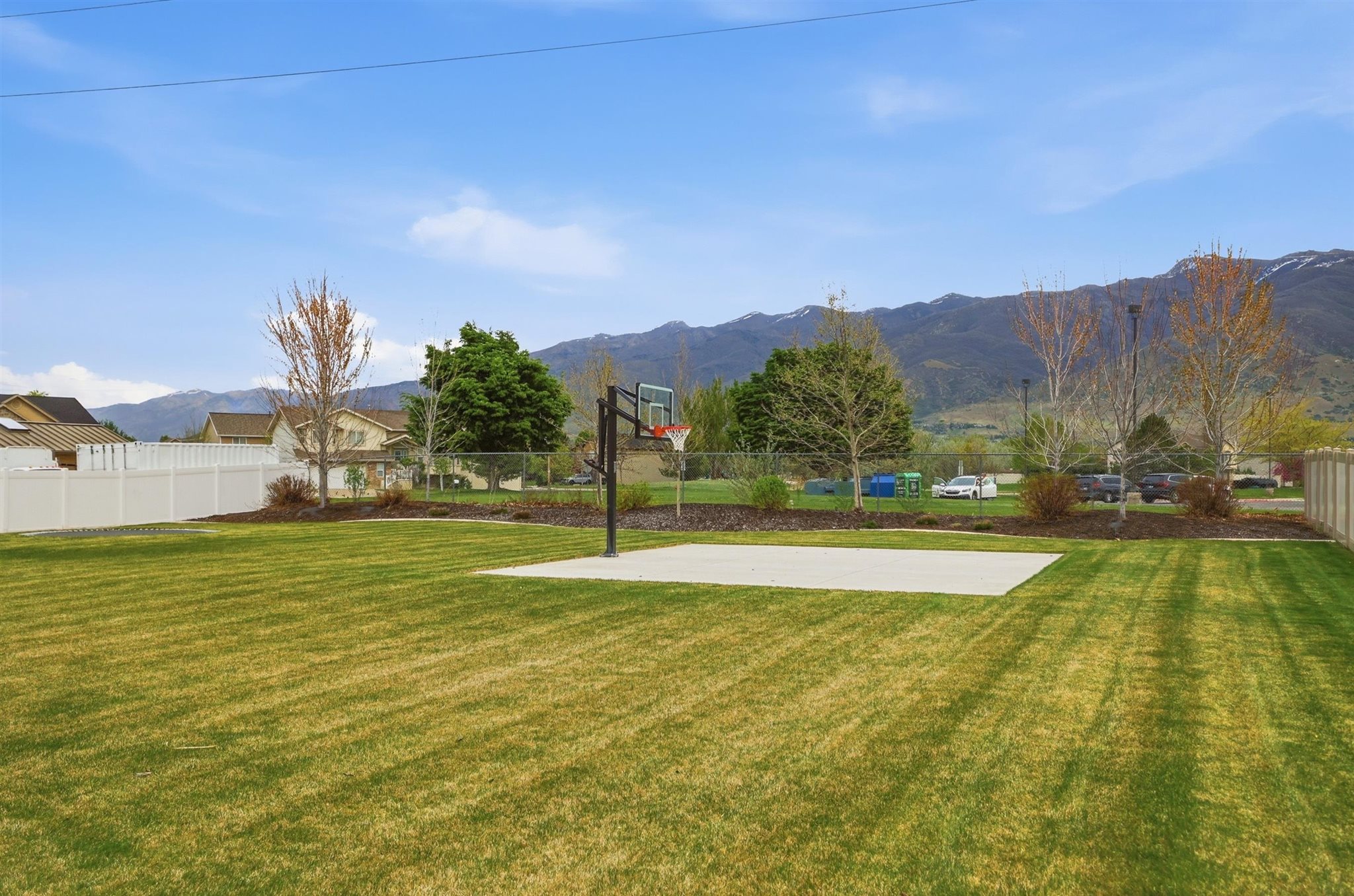 Expansive outdoor space featuring a large lawn area, a dedicated concrete pad, and a basketball hoop