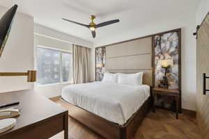 Bedroom featuring herringbone wood-finish flooring, a contemporary ceiling fan, and a paneled headboard with integrated lighting