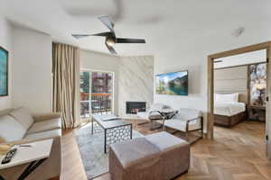 Living area featuring herringbone wood-finish flooring, a contemporary ceiling fan, and a gas fireplace with a marble-style surround