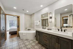 Bathroom featuring a freestanding soaking tub, dual vanity with undermount sinks, and patterned floor tiles