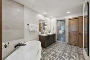 Contemporary bathroom featuring a freestanding soaking tub with a matte black faucet, a dual vanity with a white countertop, a walk-in shower with a glass enclosure, and patterned floor tiling