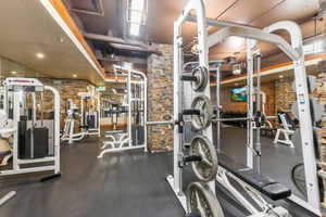 Dedicated fitness center featuring rubberized flooring, exposed industrial ceiling, stacked stone wall accents, and multiple weight machines
