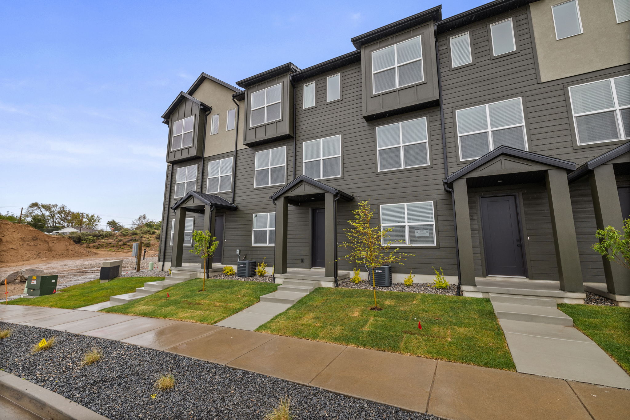 Modern townhome exterior featuring multi-level architecture, dark horizontal siding, prominent window framing, covered entryways, and concrete front walkways