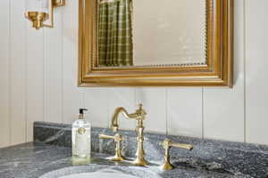 Vanity featuring a brass-finished faucet, dark stone countertop, and white vertical paneling