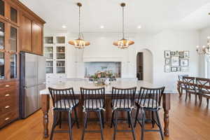 Open-concept kitchen featuring a large central island with marble countertops, cream cabinetry, integrated stainless steel refrigerator, and engineered hardwood flooring