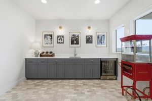 Built-in wet bar featuring gray cabinetry, granite countertops, an undermount sink, and an integrated beverage refrigerator, all set on marble tile flooring