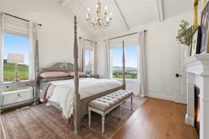 Primary bedroom with vaulted ceiling and exposed beams, hardwood flooring, and a built-in fireplace