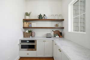 Built-in stainless steel microwave with lower cabinetry, marble countertops, and two dark wood floating shelves