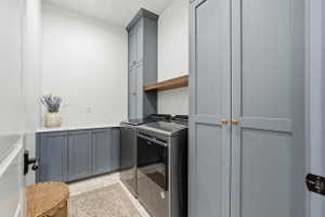 Dedicated laundry area featuring modern appliances, Portsmouth blue cabinetry, marble countertop, a tall storage cabinet, and a wood-finish floating shelf
