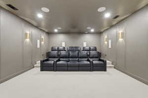 Dedicated media room featuring tiered seating, recessed ceiling lighting, wall-mounted sconces, and decorative wall paneling