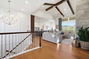 Open-concept living space featuring vaulted ceilings with exposed beams, engineered hardwood flooring, and a stone-clad fireplace
