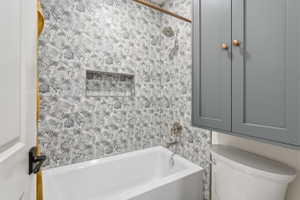 Bathtub and shower combination featuring hexagonal patterned tile walls with an integrated shower niche
