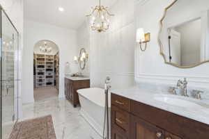 Luxurious bathroom featuring a freestanding soaking tub, dual vanity with marble countertops, polished chrome fixtures, and ornate gold-framed mirrors