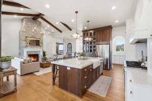Open-concept kitchen and living area featuring engineered hardwood flooring, a stone-clad fireplace, and vaulted ceilings with exposed beams