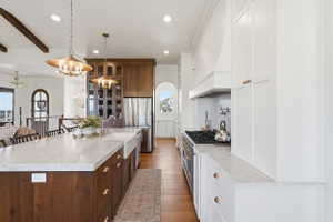 Open-concept kitchen featuring an expansive island with a farmhouse sink, marble countertops, and engineered hardood flooring
