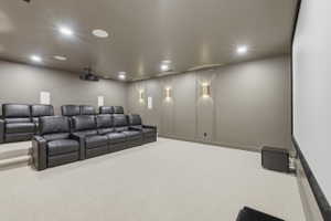 Dedicated home theater featuring tiered seating, a large projection screen, recessed ceiling lighting, and decorative wall sconces