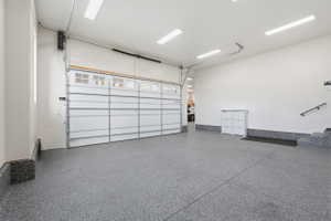 Spacious garage featuring a durable epoxy-coated floor, bright overhead lighting, and a paneled garage door with upper window inserts