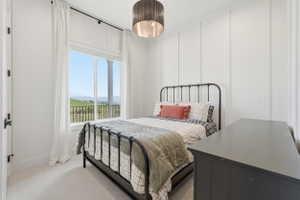 Bedroom featuring a large window, white board and batten accent wall, neutral carpet flooring, a dark drum pendant light fixture, and black hardware on the door