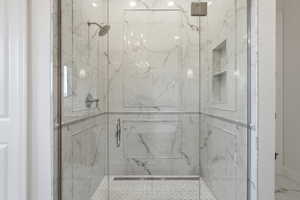 Frameless glass shower enclosure featuring marble-like tile walls with decorative trim, a built-in shower niche, a rain shower head, and a hexagonal mosaic tile floor