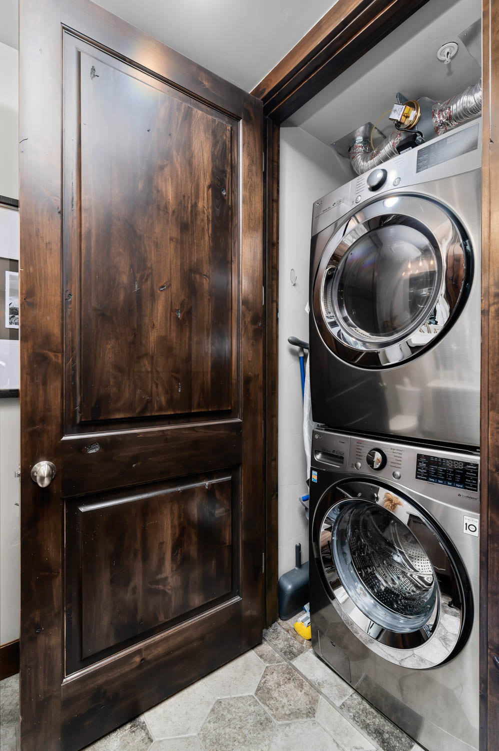 Dedicated laundry closet featuring a stacked washer and dryer, hexagon tile flooring, and a rich wood-finish door with brushed nickel hardware