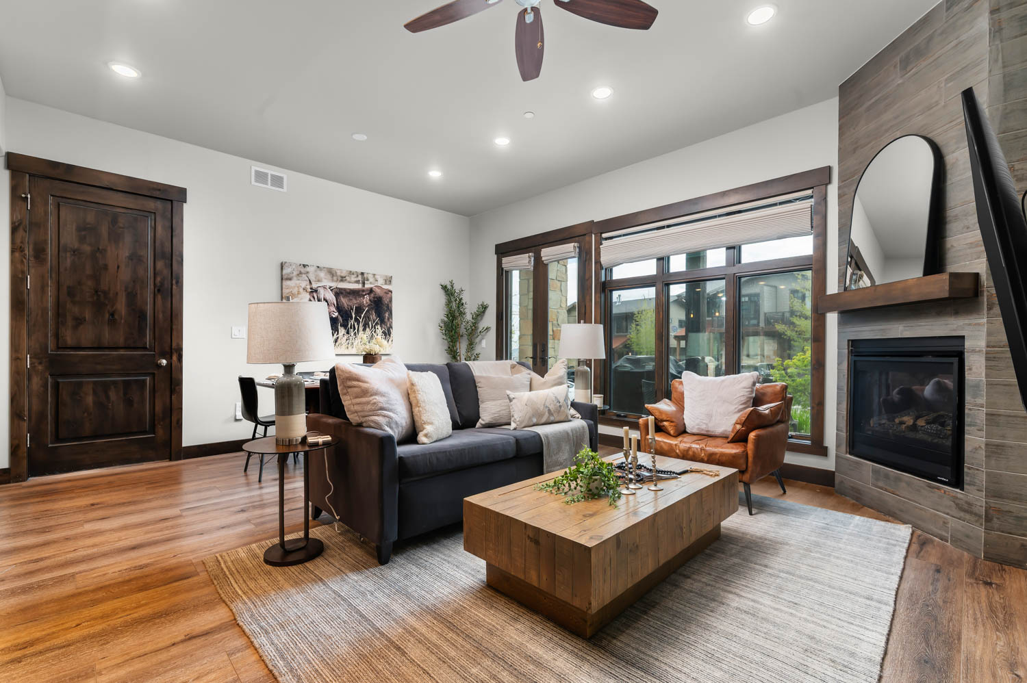 Living area featuring wood-finish flooring, a contemporary gas fireplace with a tiled surround, recessed lighting, and large windows with dark wood trim