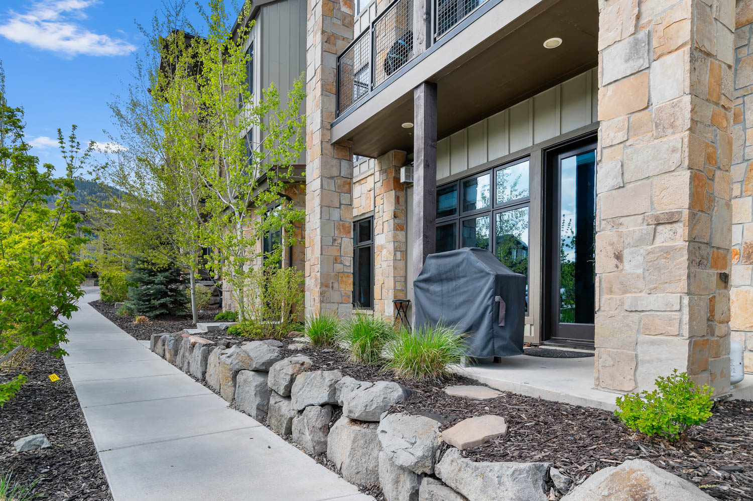 Stone exterior with a concrete patio, featuring large windows and a glass-paneled door