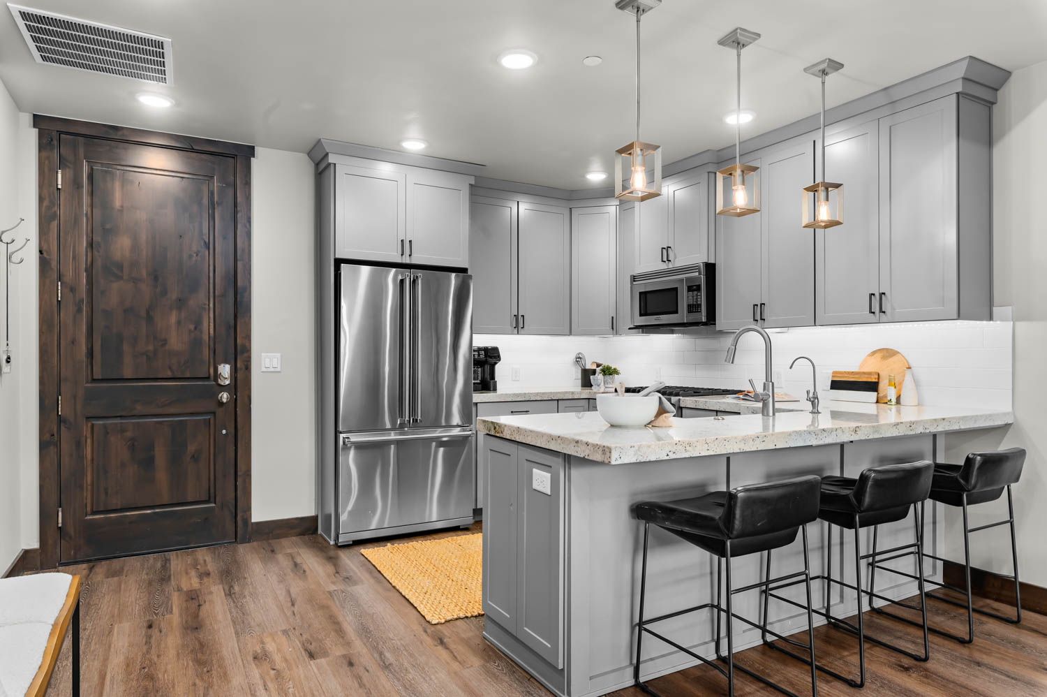Gourmet kitchen featuring light gray cabinetry, stainless steel appliances, a white subway tile backsplash, and wood-finish flooring