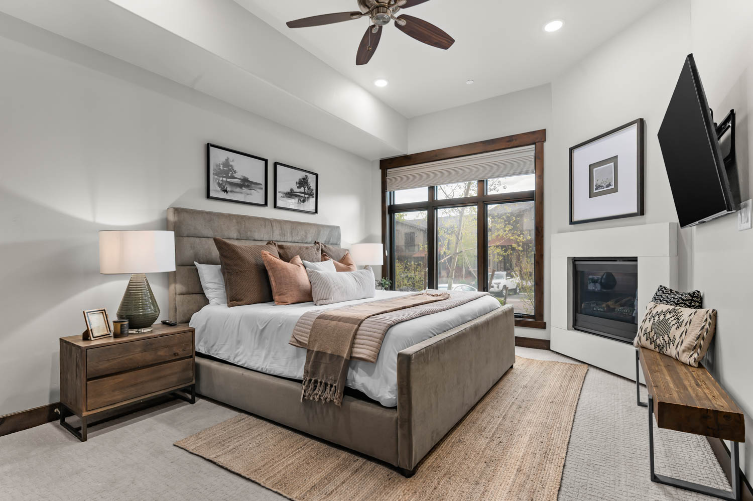 Bedroom featuring a built-in corner fireplace, large window with dark wood trim, recessed ceiling lighting, and a ceiling fan