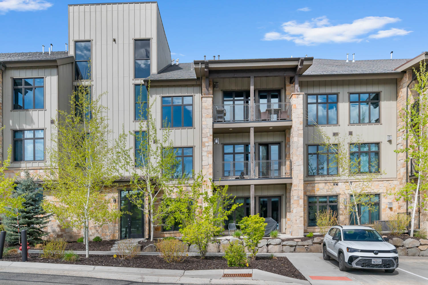 Contemporary multi-level building featuring a mix of vertical siding, stucco, and stone veneer accents