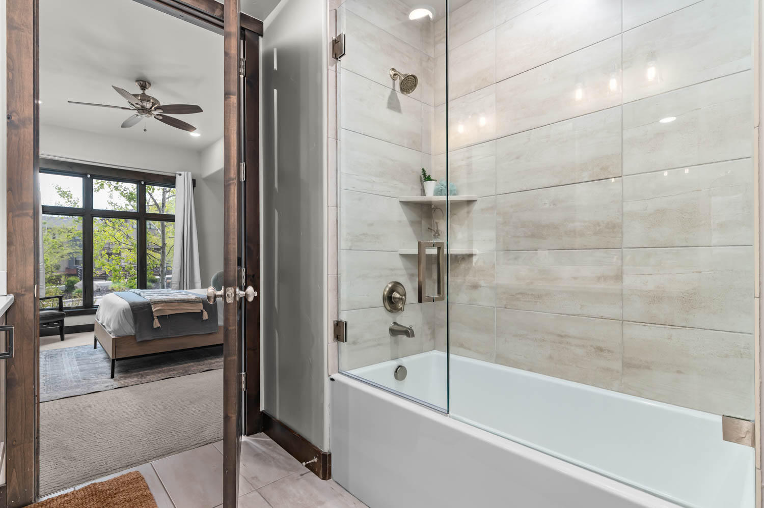 Bathroom featuring a tub and shower combination with glass enclosure, light-toned tile surround, and brushed nickel fixtures