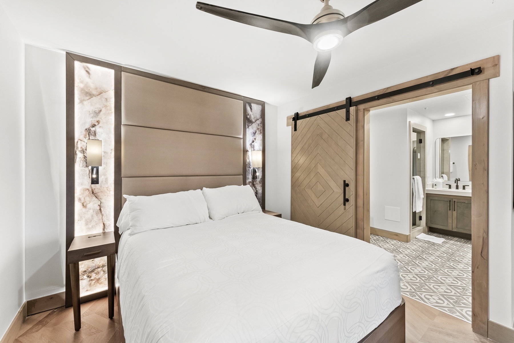 Bedroom featuring a statement headboard with integrated lighting, wood-finish flooring, and a ceiling fan