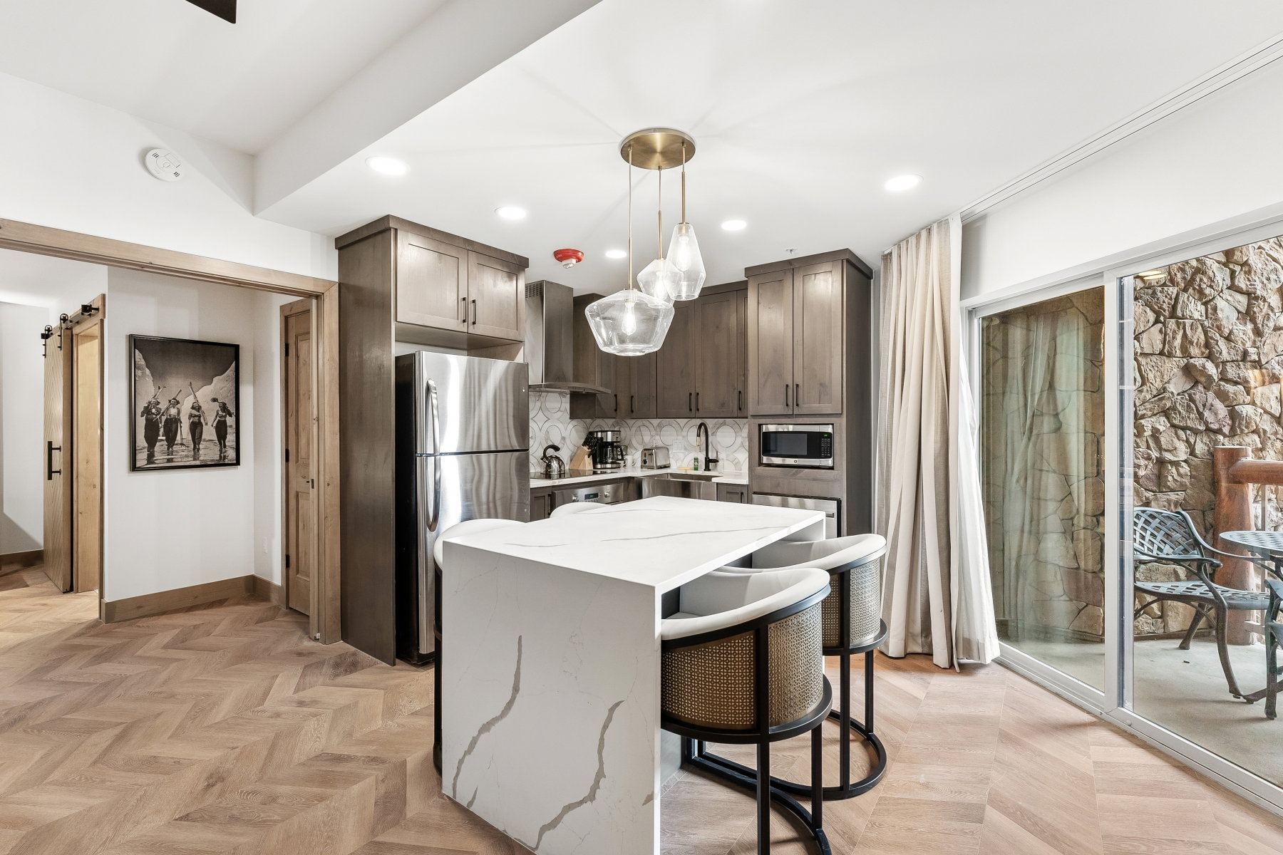 Modern kitchen featuring a waterfall island, herringbone wood-finish flooring, stainless steel appliances, and dark wood cabinetry