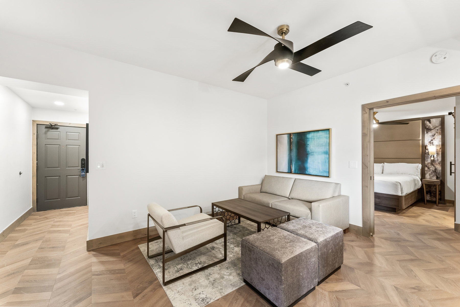 Open-concept living area featuring herringbone wood-finish flooring, a contemporary ceiling fan, and a wide entryway to a separate room
